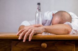 man passes out on the table with an empty alcohol bottle after binge drinking