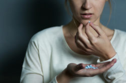 woman taking a Xanax pill while several blue pills are on her palm