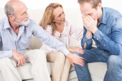 adult man with substance abuse issues cries while confessing to his elderly parents 