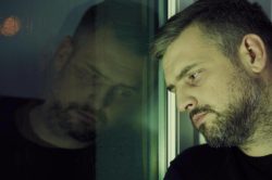 depressed, addicted  man leans on a glass window 