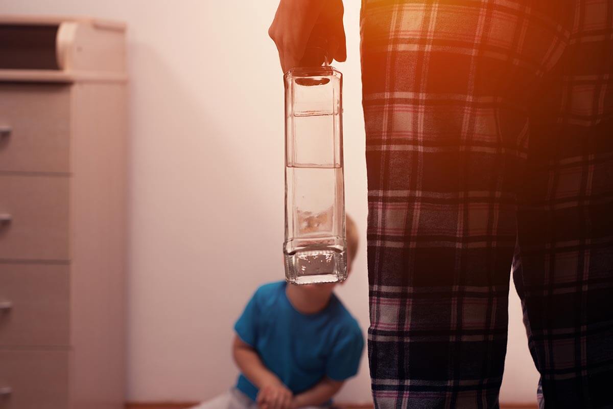 lighthousetreatment-alcoholism-and-genetics-what-you-need-to-know-article-photo-drunk-mother-with-bottle-and-scared-little-son-sitting-on-the-floor-alcoholic-addiction-519412576