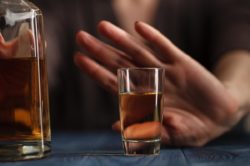 a woman's hand refusing a shot of whiskey