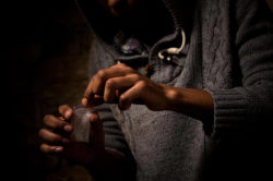 closeup of a man's hand wearing a grey hoodie opening a small plastic bag containing cocaine