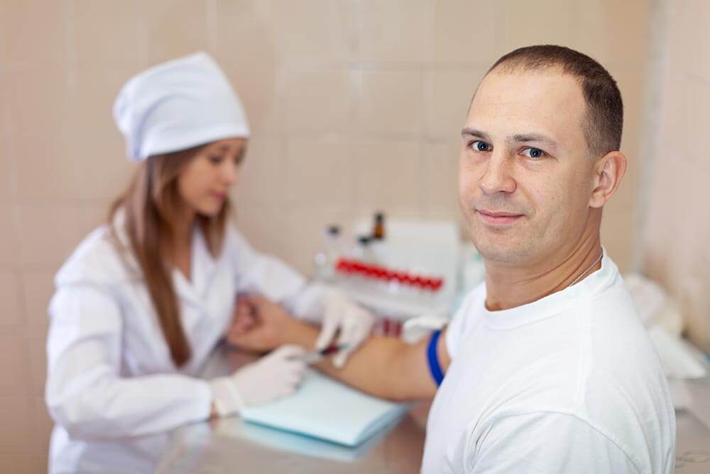 man looking at camera while a nurse draws blood during a test for opiates