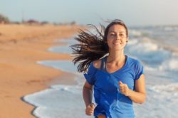 a smiling woman with her headphones while running on the beach