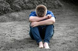 a bullied teen sits on the concrete sidewalk