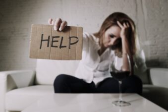 Alcoholic woman holding out a HELP sign made of cardboard